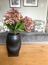 Load image into Gallery viewer, A shaped matt black vase, with a smooth, curved exterior ideal for faux flowers 
